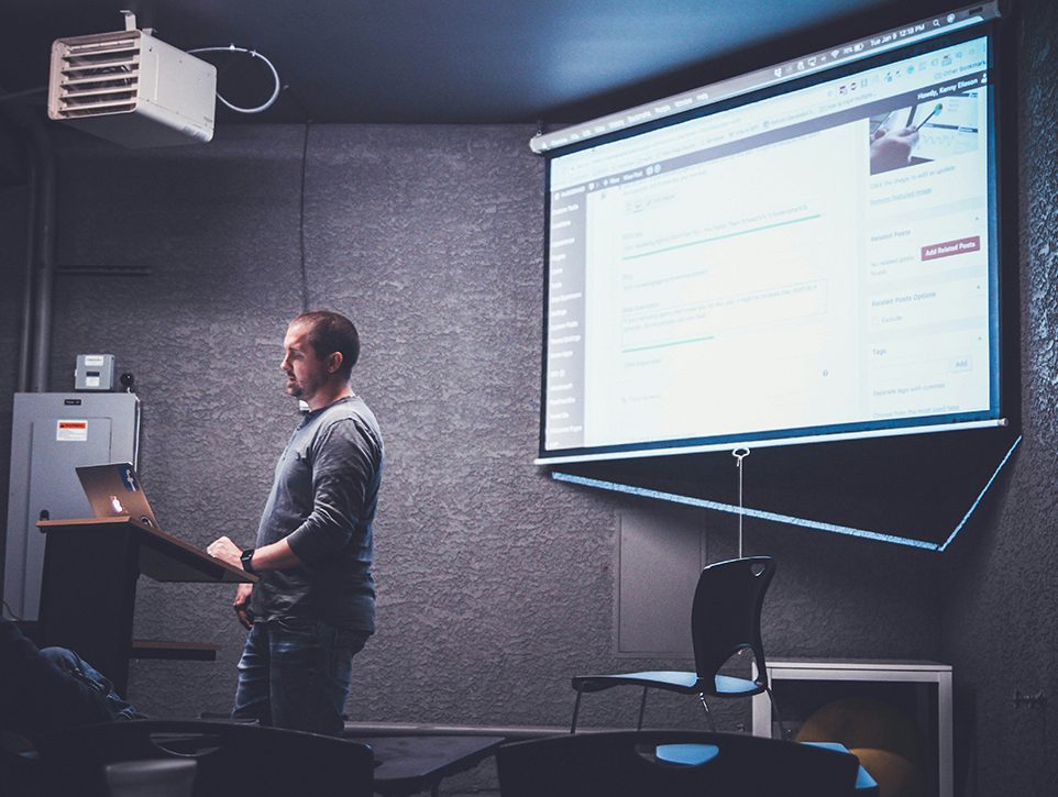 A man standing in front of a projector screen.