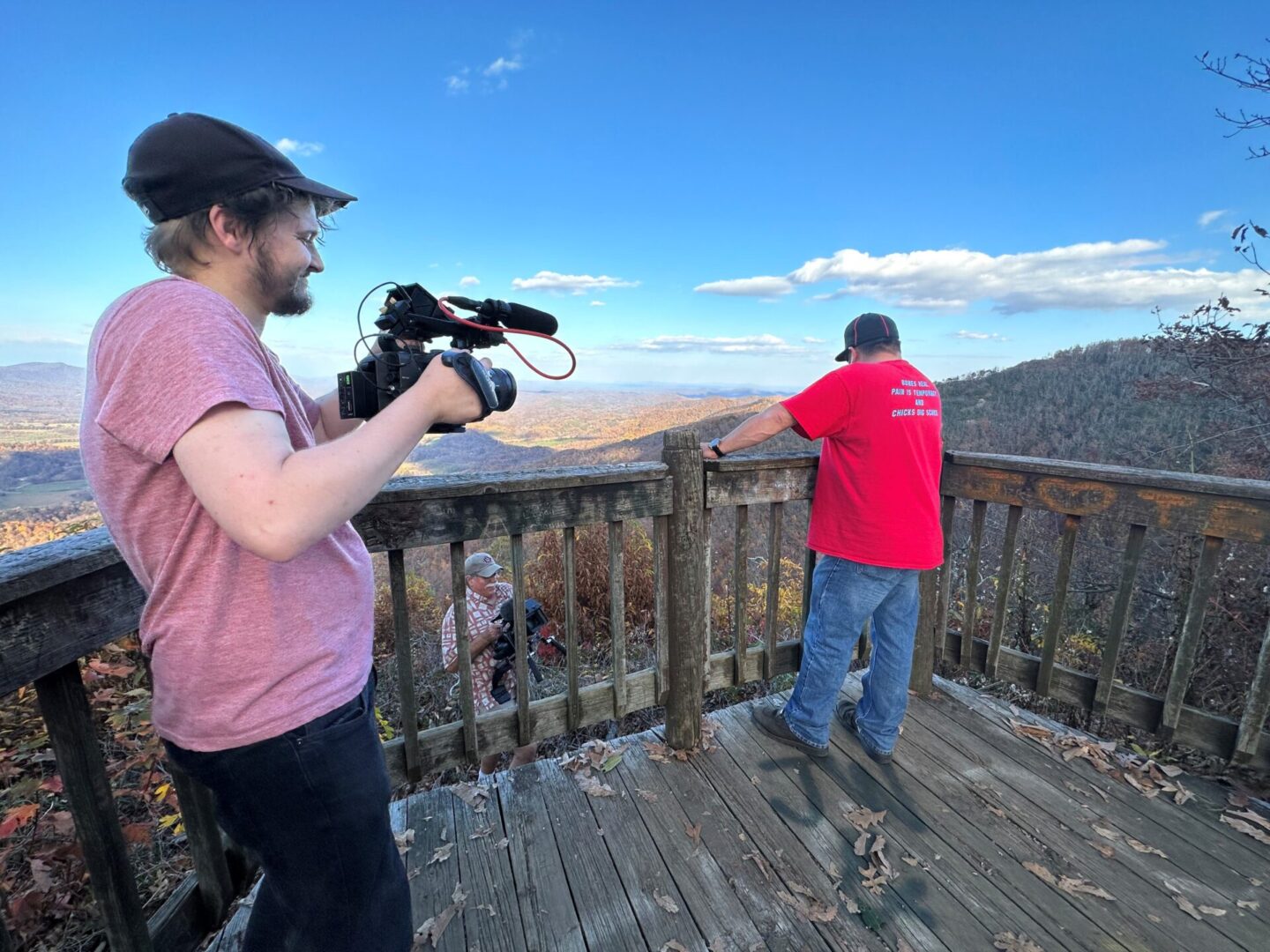 A man holding a camera while standing on top of a wooden deck.